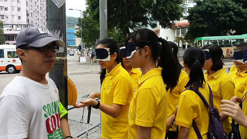 Visually impaired public education ambassador leading blind-folded participants for a blind experience on the street