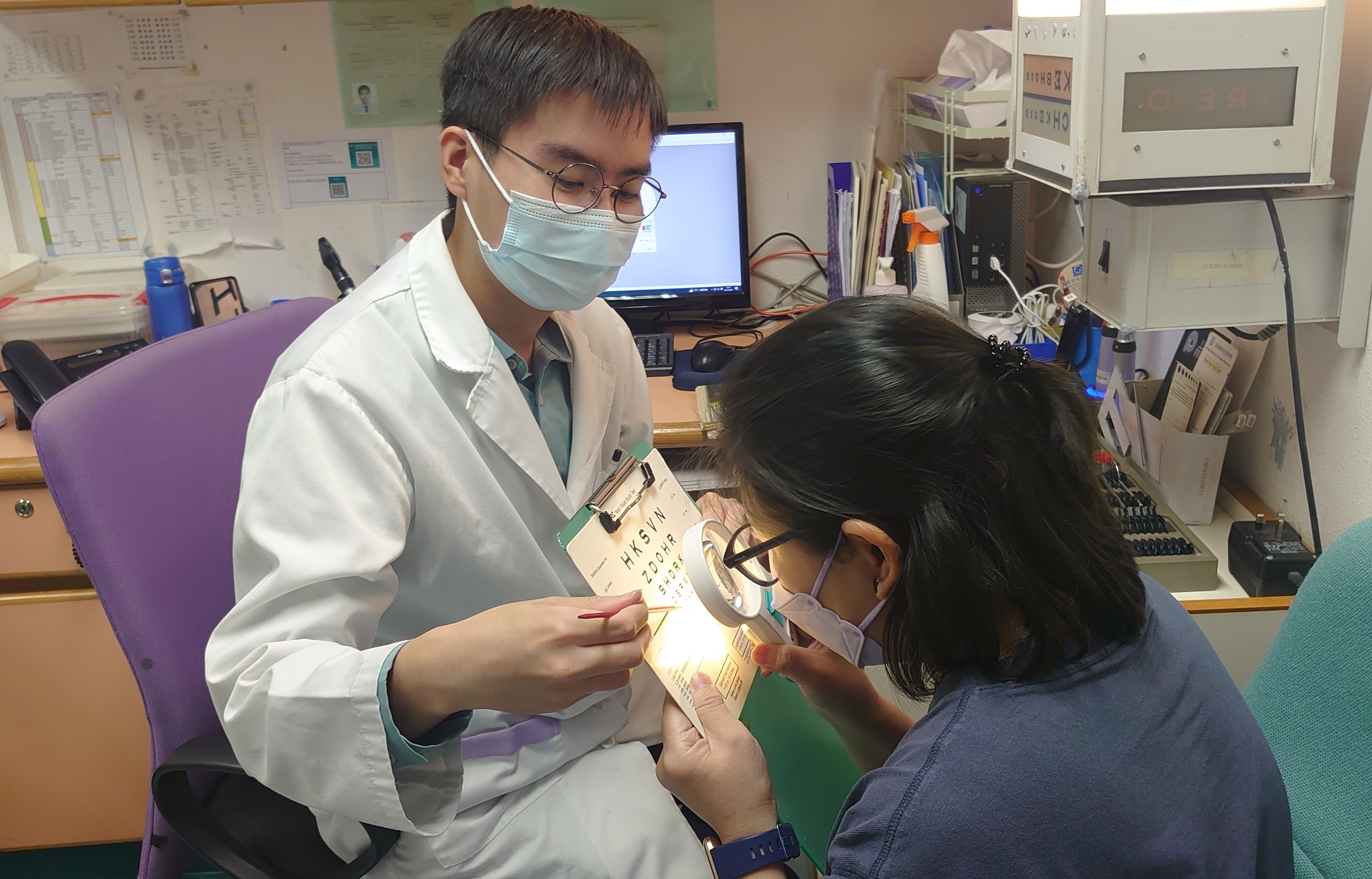 An optometrist demonstrates to a patient how to use a hand-held magnifier.
